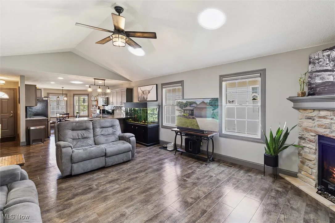 Living area with a ceiling fan, dark wood-type flooring, a fireplace, and lofted ceiling