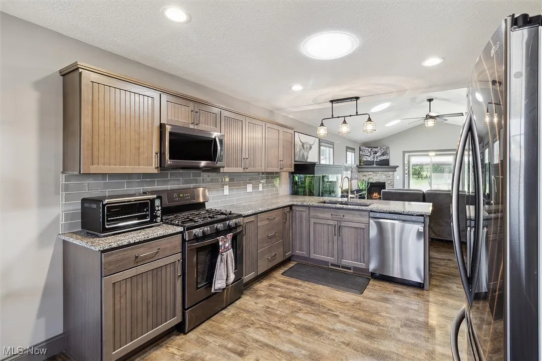 Kitchen featuring appliances with stainless steel finishes, ceiling fan, light wood-type flooring, vaulted ceiling, and light stone counters