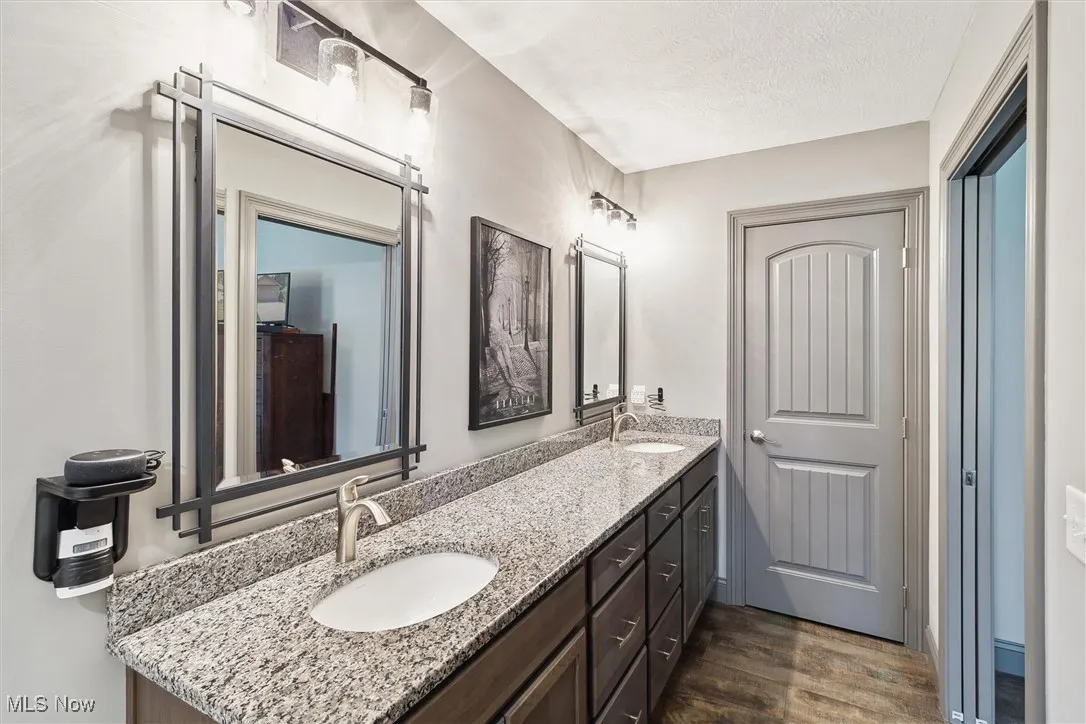 Full bath featuring double vanity, wood finished floors, and a textured ceiling