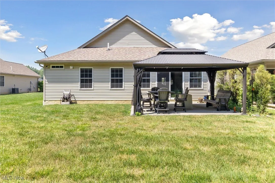 Back of property with a gazebo, a patio area, a lawn, and roof with shingles