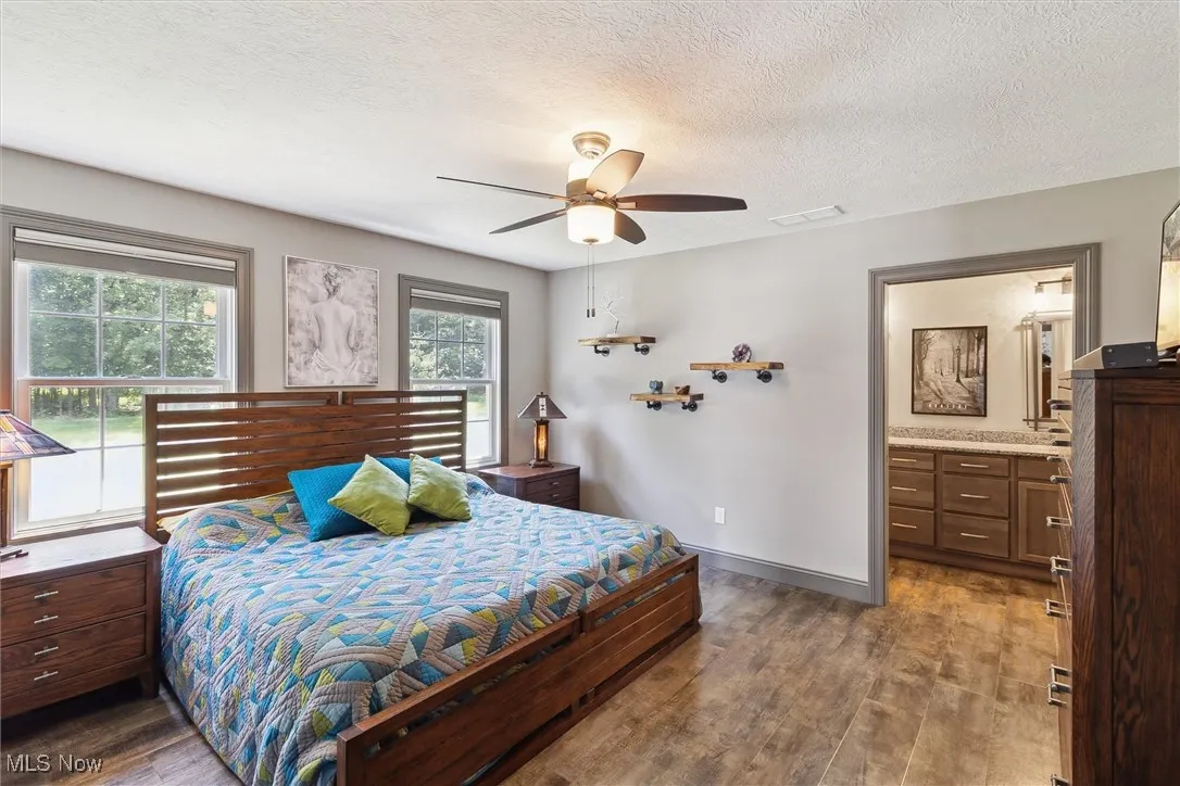 Bedroom with wood finished floors, a textured ceiling, connected bathroom, and a ceiling fan