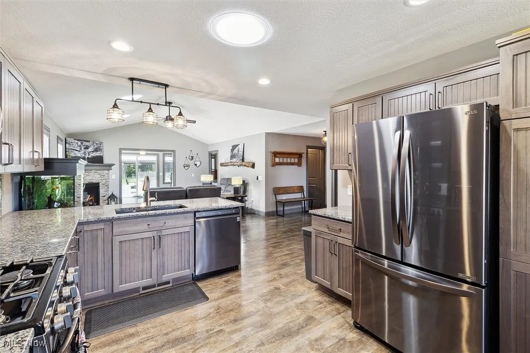 Kitchen featuring stainless steel appliances, vaulted ceiling, light wood-style flooring, a peninsula, and open floor plan
