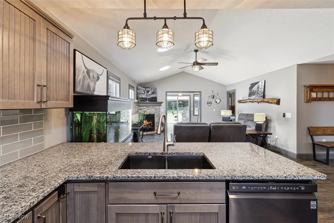 Kitchen featuring lofted ceiling, ceiling fan, dishwasher, light stone countertops, and a stone fireplace