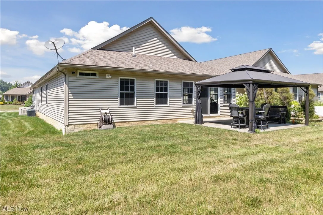 Rear view of house featuring a gazebo, a patio area, a lawn, and a shingled roof