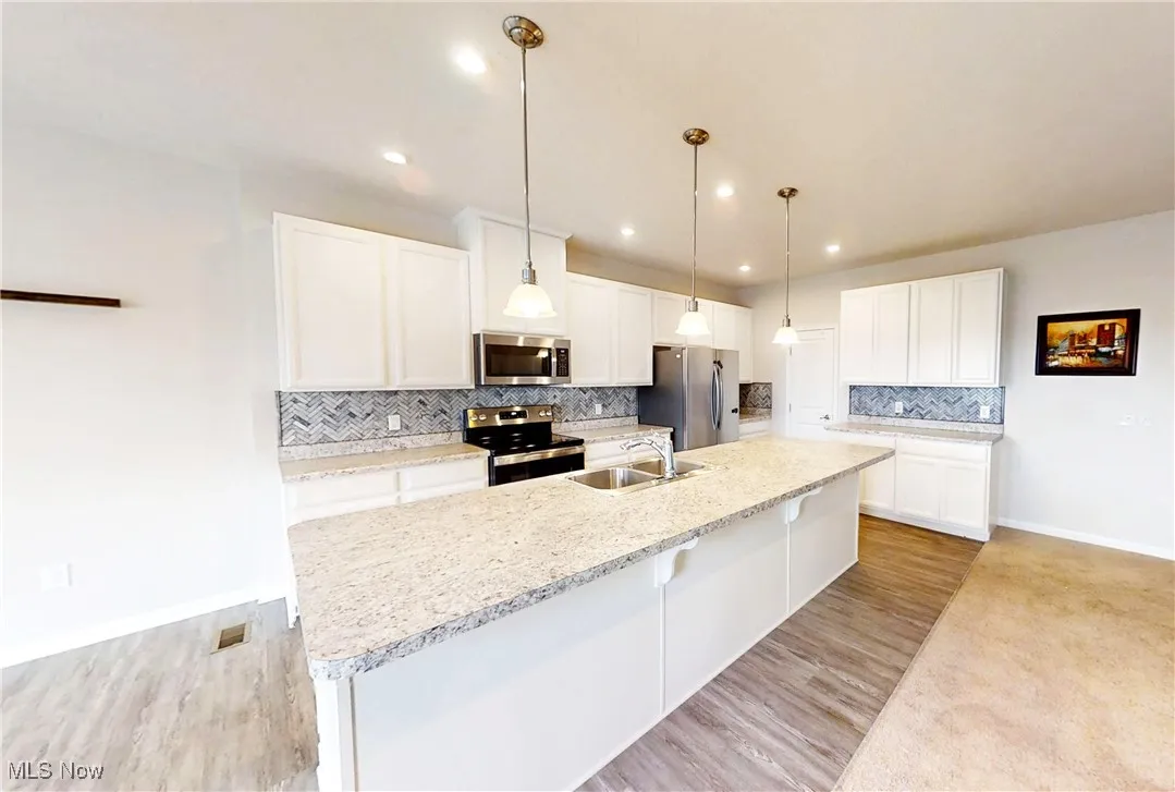 Kitchen with stainless steel appliances, a spacious island, decorative backsplash, white cabinetry, and recessed lighting