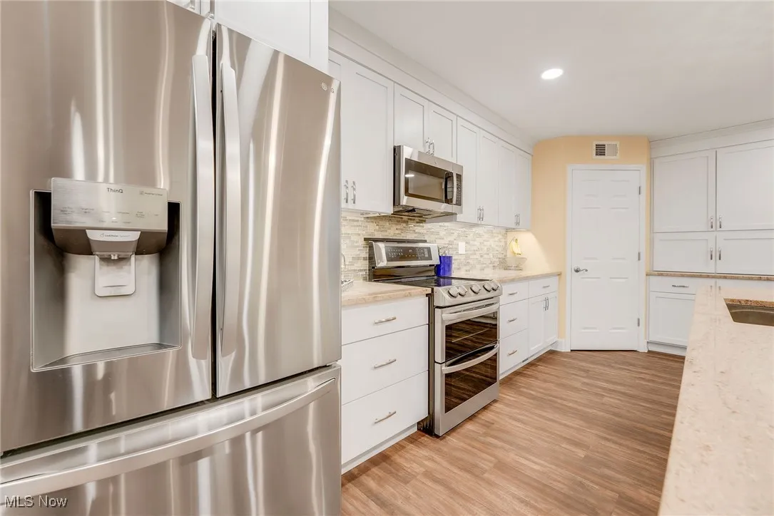 Kitchen featuring appliances with stainless steel finishes, white cabinets, backsplash, luxury vinyl floors, and recessed led lighting open shelving and large island with breakfast bar