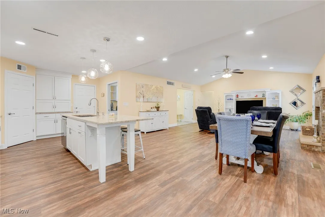 Dining room featuring luxary vinyl flooring, a ceiling fan, lofted ceiling, a gas fireplace, and a chandelier