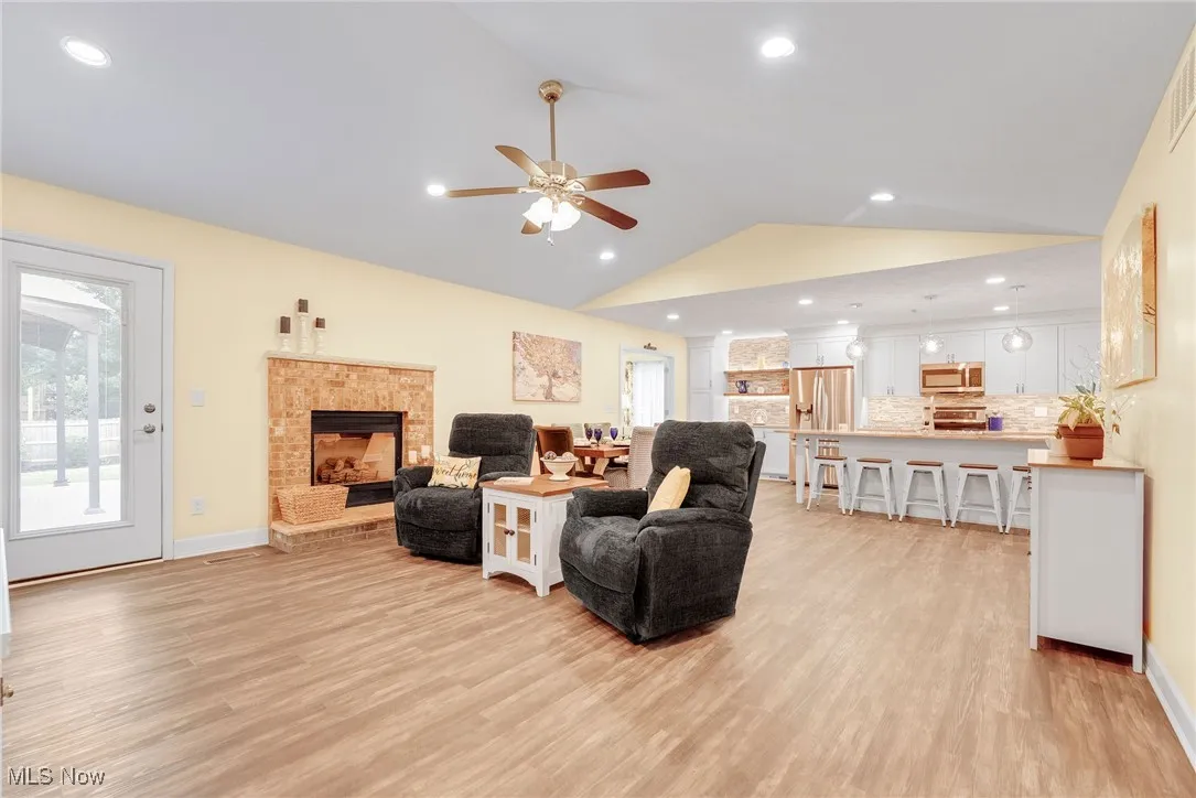 Living area featuring vaulted ceiling, luxury vinyl floors, a ceiling fan, a fireplace, and healthy amount of natural light