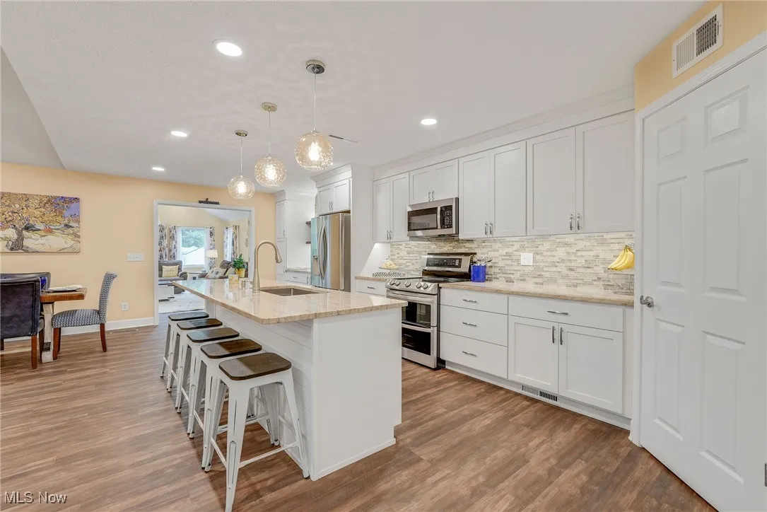 Kitchen featuring appliances with stainless steel finishes,  luxury vinyl finished floors, a kitchen bar, and white shaker cabinetry, walk in pantry, open shelving and so more more.