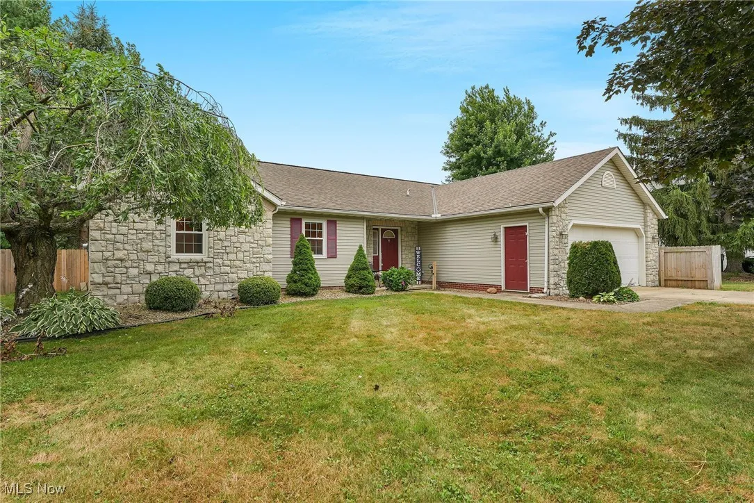 Ranch-style home with stone siding, driveway, an attached garage, and a shingled roof