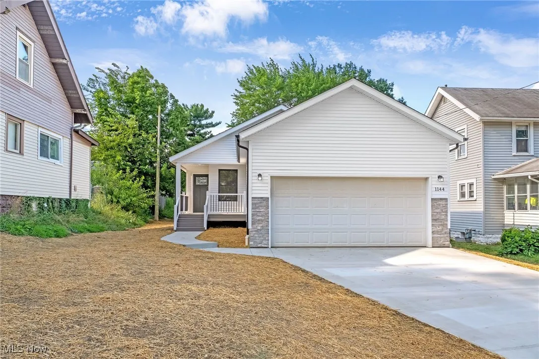 View of front of house featuring stone siding, an attached garage, driveway, and covered porch