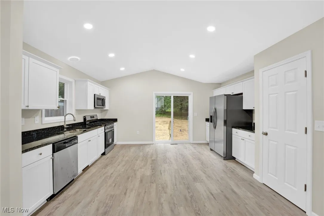 Kitchen featuring stainless steel appliances, lofted ceiling, white cabinets, light wood-style floors, and recessed lighting