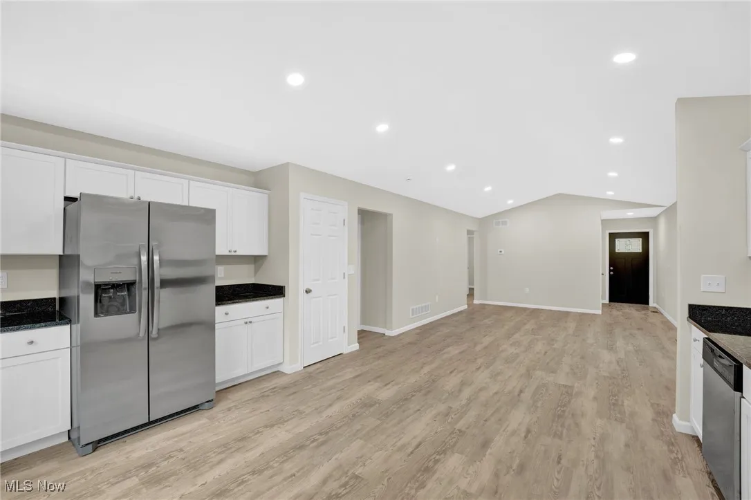 Kitchen with appliances with stainless steel finishes, white cabinetry, light wood finished floors, vaulted ceiling, and dark stone countertops