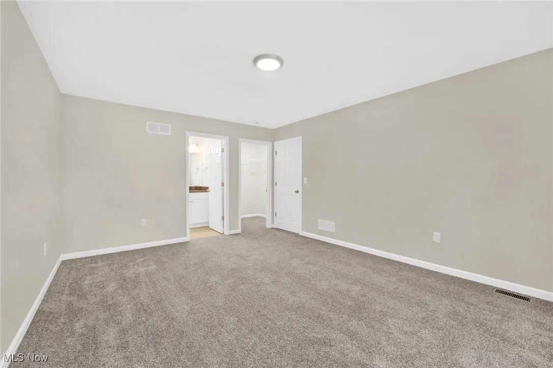 Unfurnished bedroom featuring light carpet, ensuite bathroom, and a spacious closet