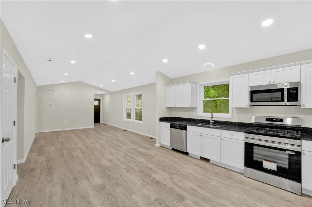 Kitchen featuring appliances with stainless steel finishes, lofted ceiling, white cabinetry, light wood-style floors, and open floor plan