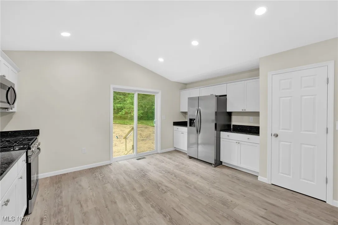 Kitchen featuring appliances with stainless steel finishes, white cabinets, light wood-style flooring, lofted ceiling, and recessed lighting