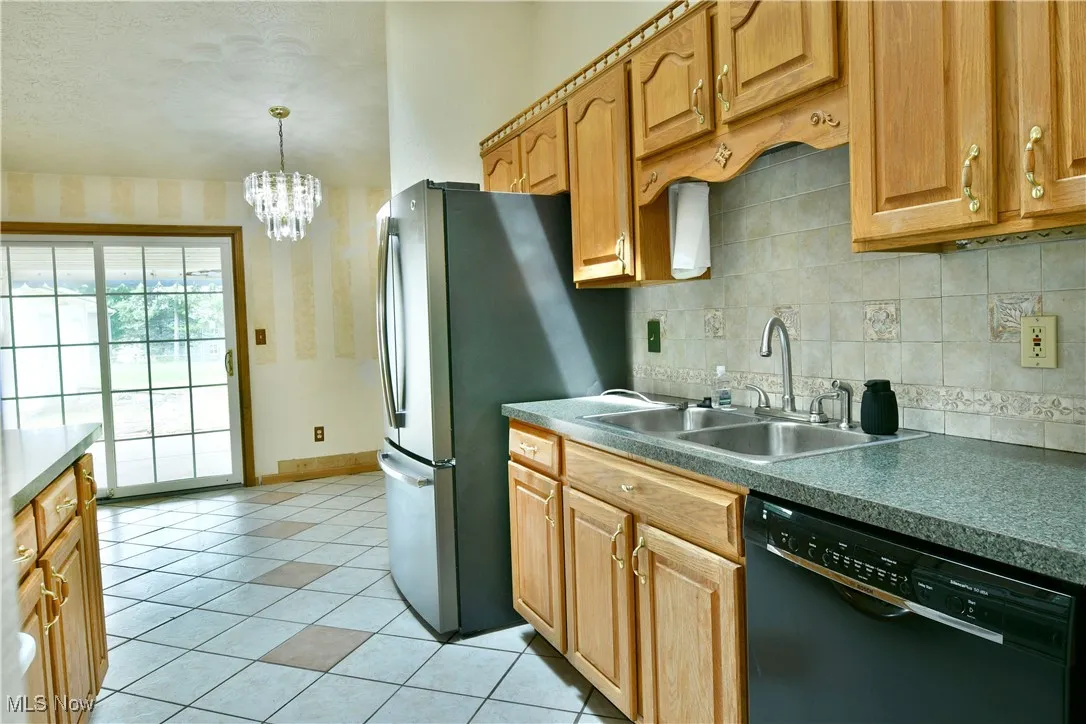 Kitchen with black dishwasher, light tile patterned flooring, backsplash, freestanding refrigerator, and a chandelier