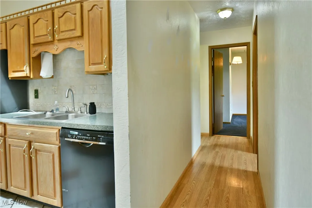 Kitchen with black dishwasher, light wood finished floors, decorative backsplash, and light countertops