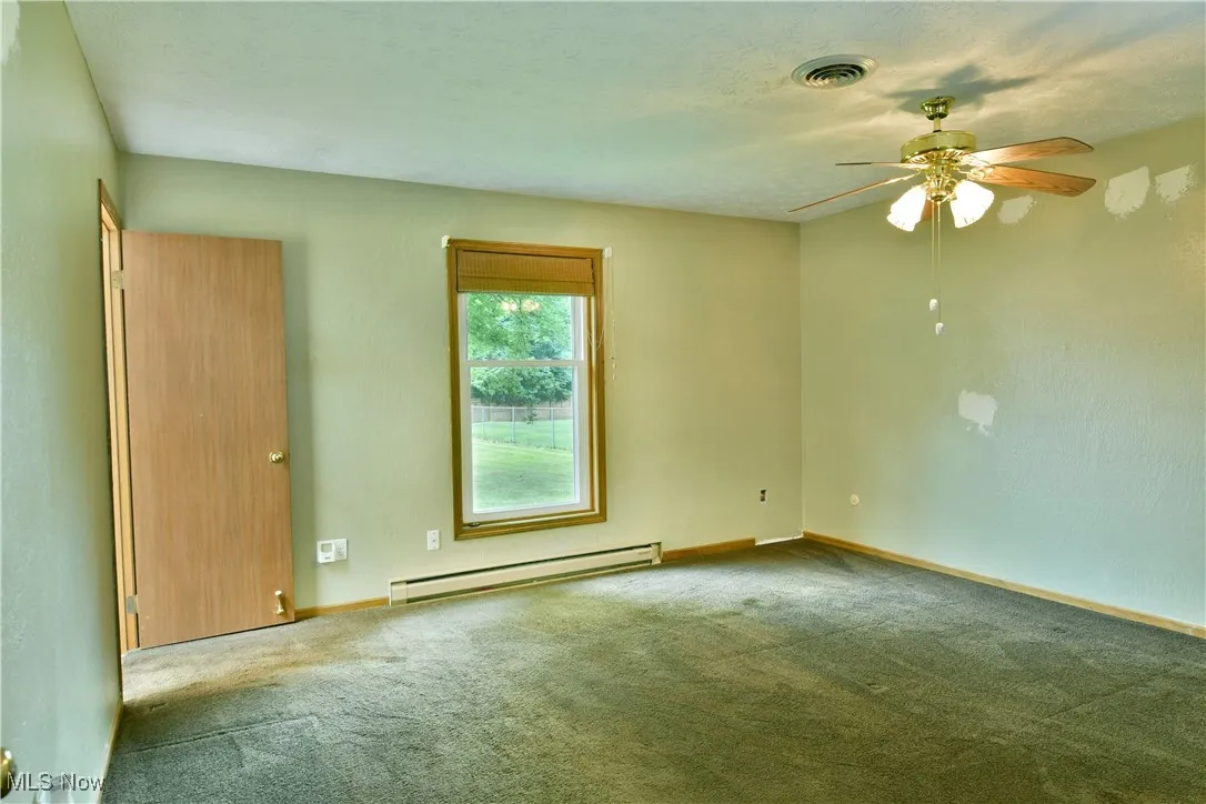 Carpeted spare room with baseboard heating and ceiling fan