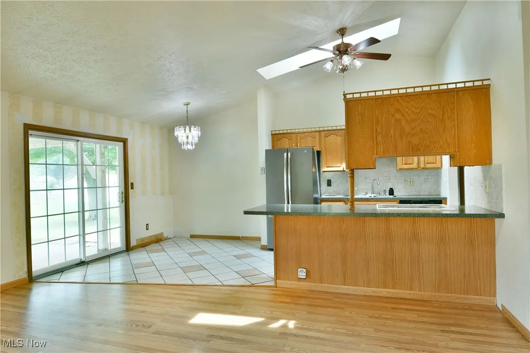 Kitchen with a skylight, a peninsula, dark countertops, lofted ceiling, and light wood finished floors