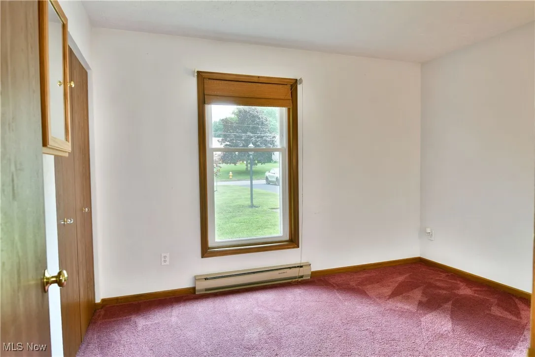 Empty room featuring a baseboard heating unit and carpet flooring