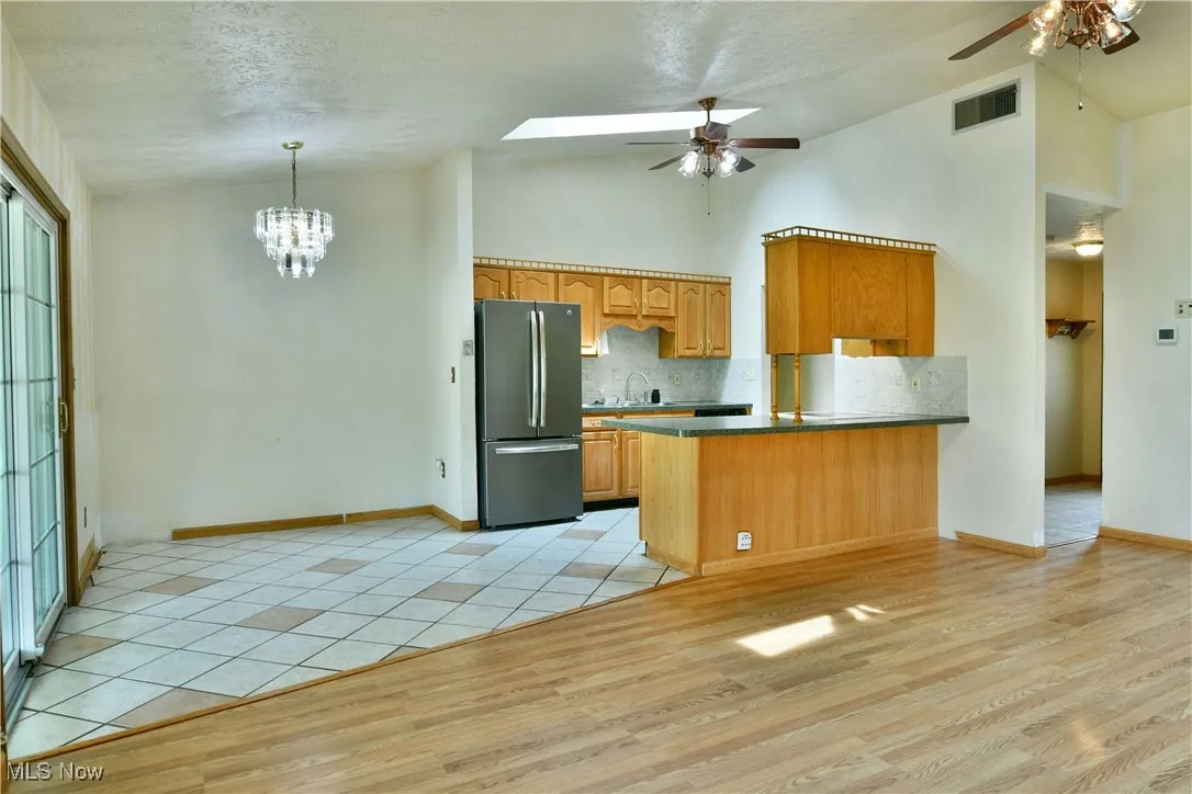 Kitchen featuring ceiling fan, freestanding refrigerator, light wood-style flooring, backsplash, and a peninsula