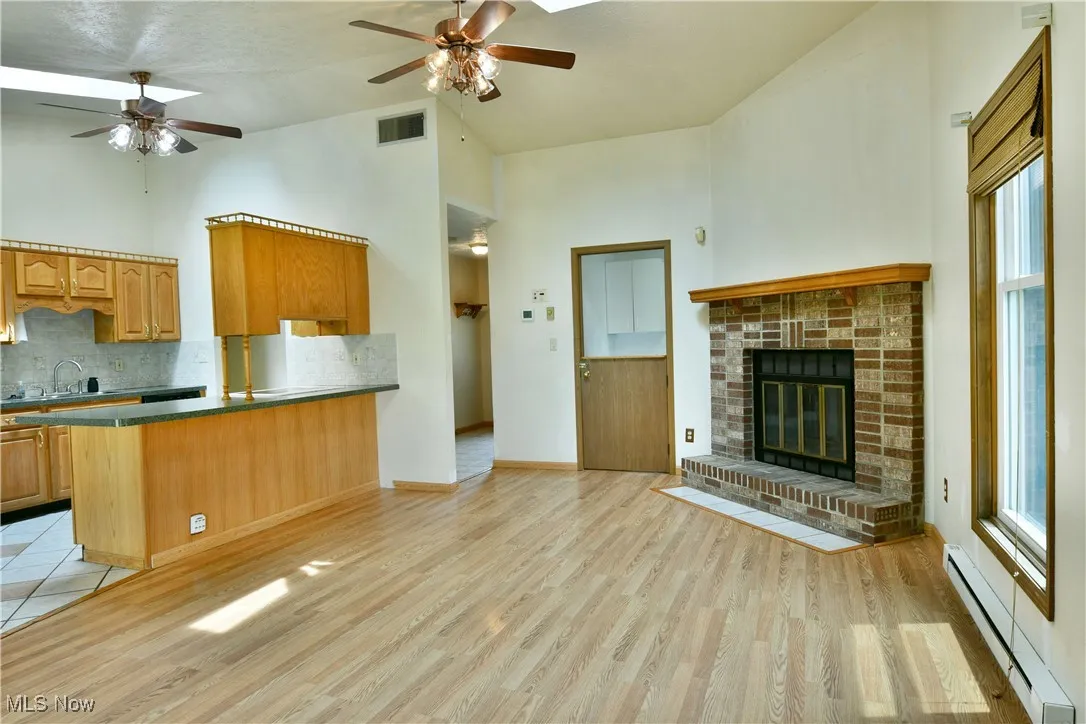 Kitchen featuring ceiling fan, baseboard heating, open floor plan, high vaulted ceiling, and decorative backsplash
