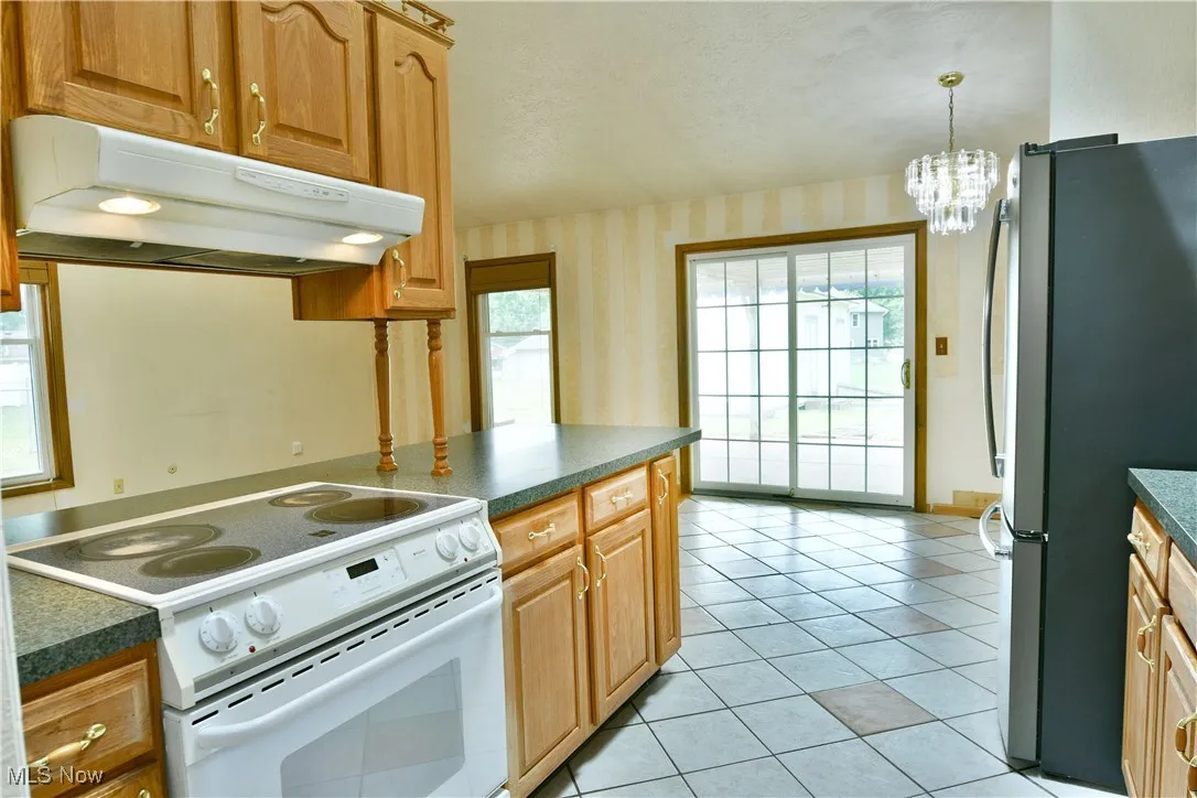 Kitchen featuring wallpapered walls, electric range, under cabinet range hood, freestanding refrigerator, and dark countertops