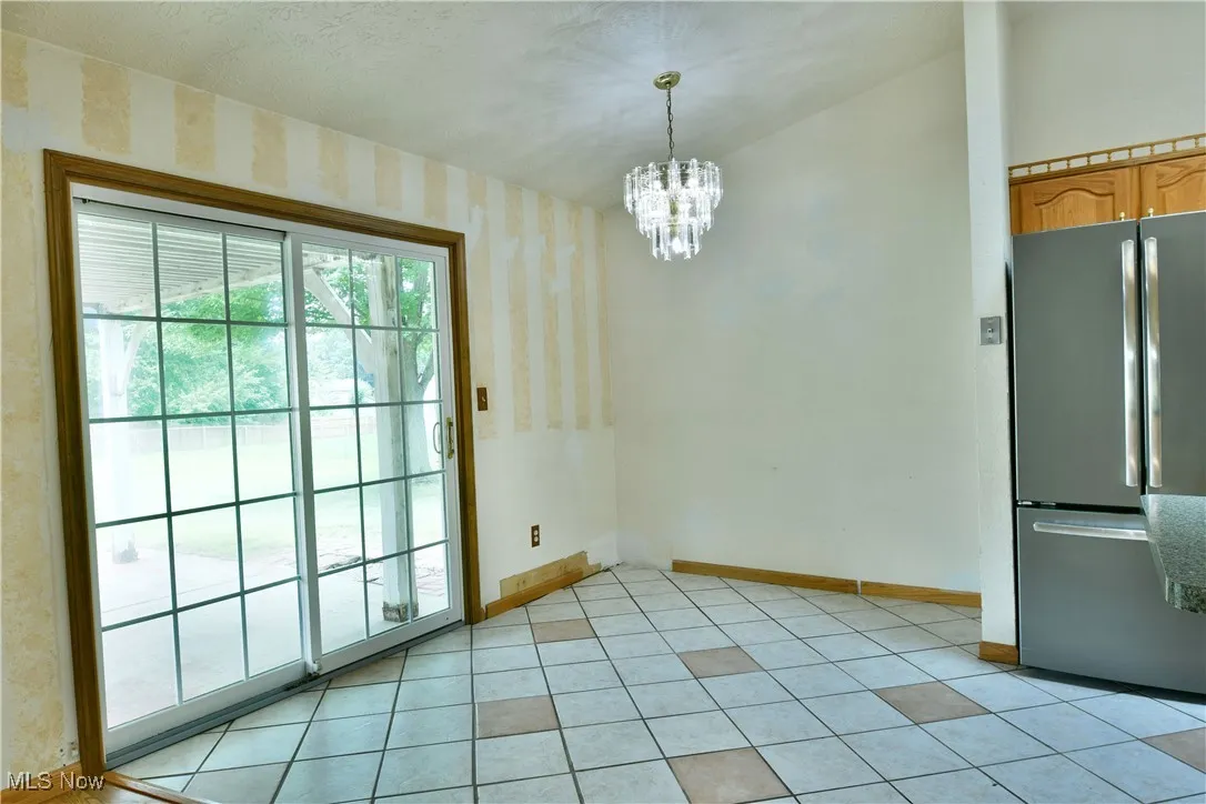 Unfurnished dining area featuring wallpapered walls, a chandelier, and light tile patterned flooring