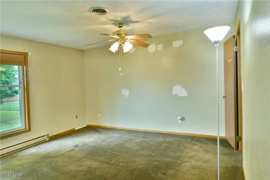 Carpeted empty room featuring a ceiling fan and baseboard heating