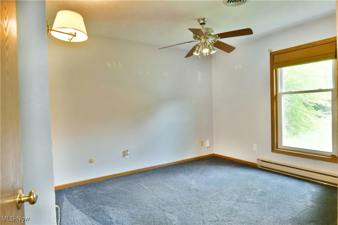 Spare room featuring a baseboard heating unit, carpet, and ceiling fan