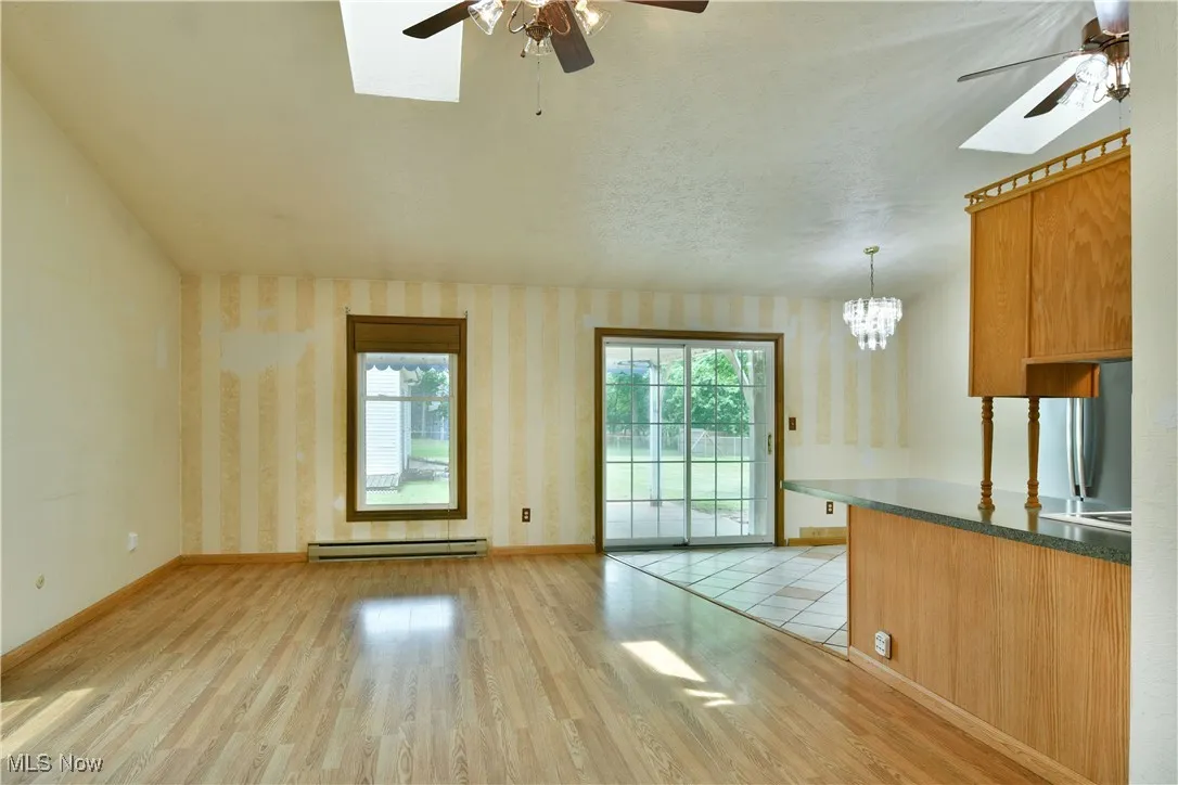 Unfurnished living room featuring a ceiling fan, a skylight, wallpapered walls, and light wood finished floors
