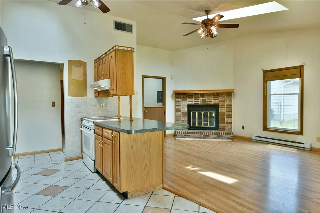 Kitchen featuring a ceiling fan, dark countertops, electric range, a baseboard heating unit, and stainless steel refrigerator
