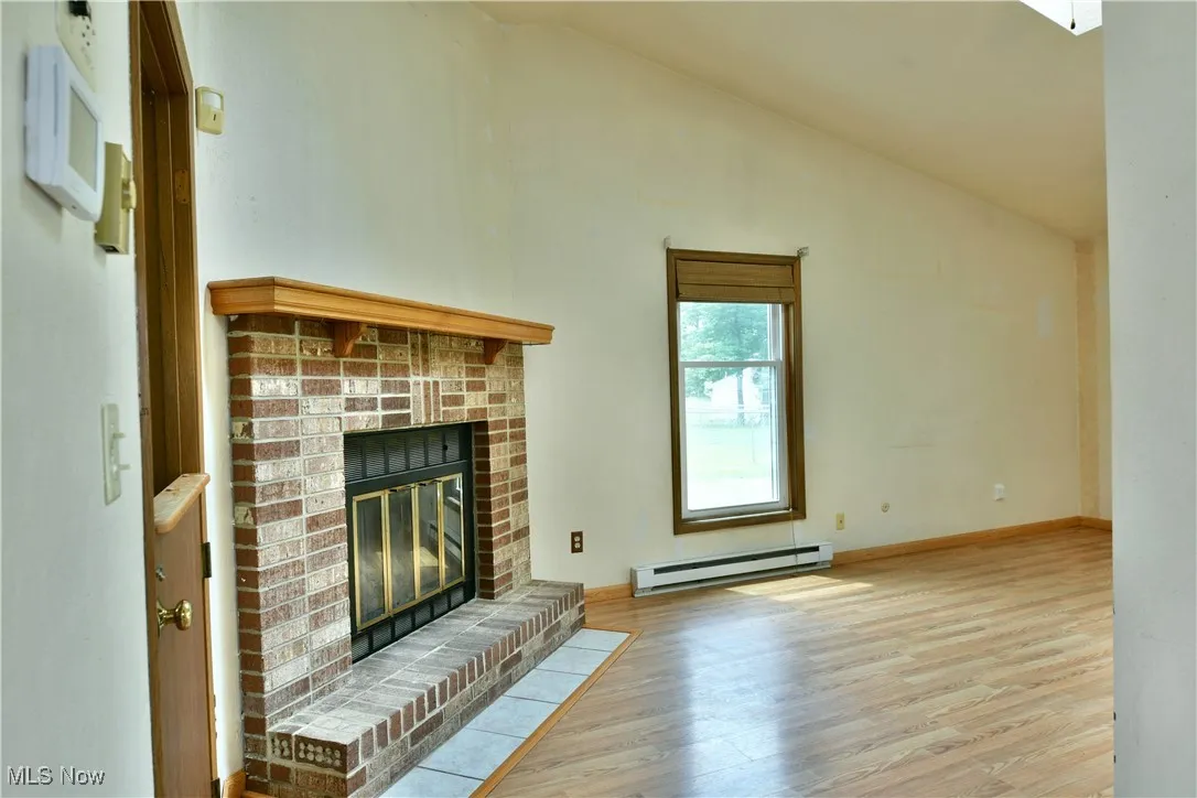 Unfurnished living room featuring wood finished floors, a fireplace, baseboard heating, and high vaulted ceiling