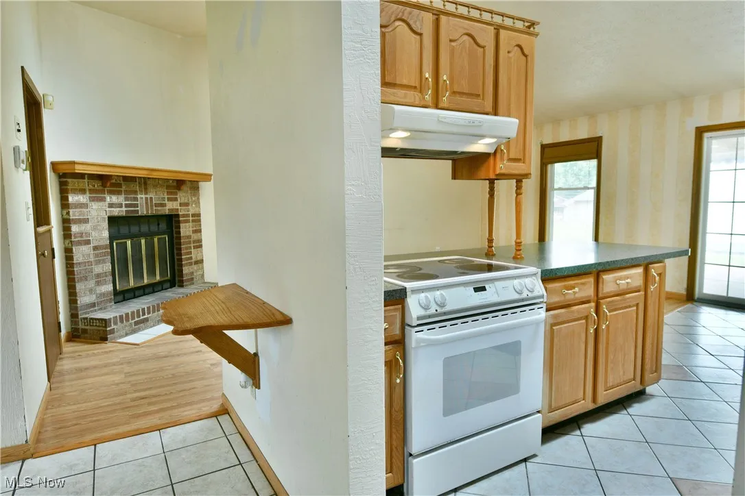 Kitchen with white range with electric stovetop, under cabinet range hood, light tile patterned floors, wallpapered walls, and dark countertops