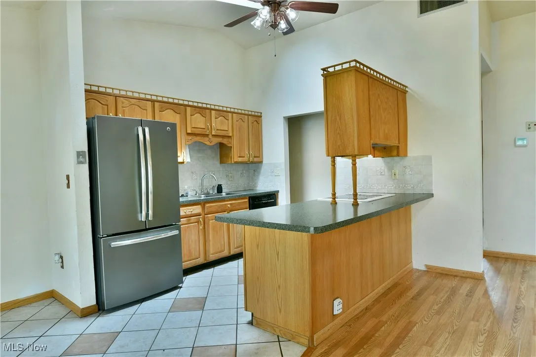 Kitchen featuring freestanding refrigerator, dark countertops, a ceiling fan, backsplash, and high vaulted ceiling