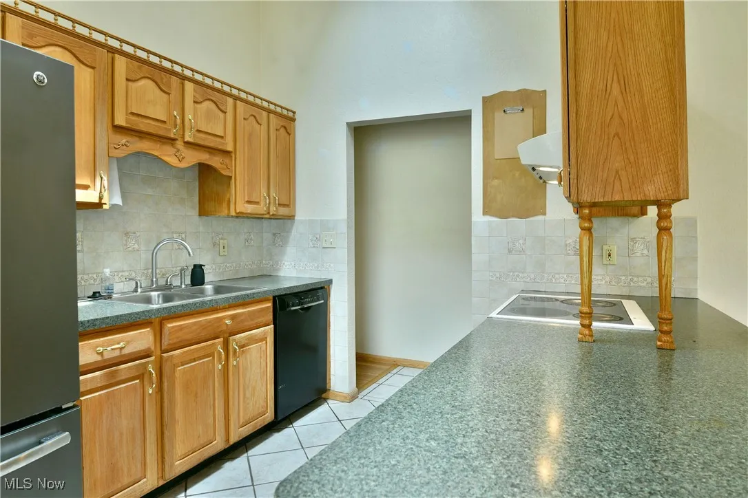 Kitchen featuring freestanding refrigerator, decorative backsplash, dishwasher, dark countertops, and a high ceiling