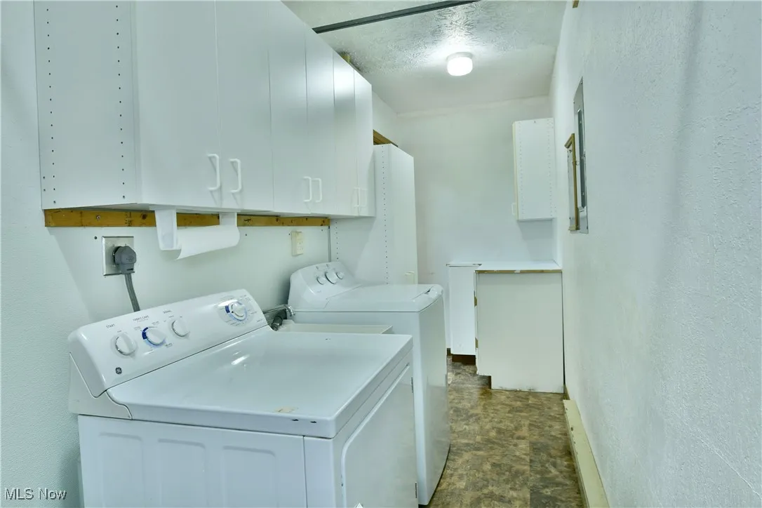 Laundry area with cabinet space, washing machine and clothes dryer, stone finish flooring, and a textured ceiling