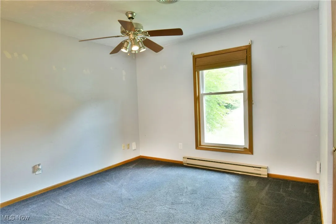 Carpeted empty room featuring a baseboard radiator and ceiling fan