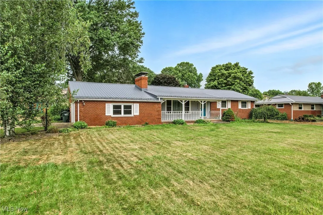 Single story home featuring brick siding, a chimney, a metal roof, and a front yard