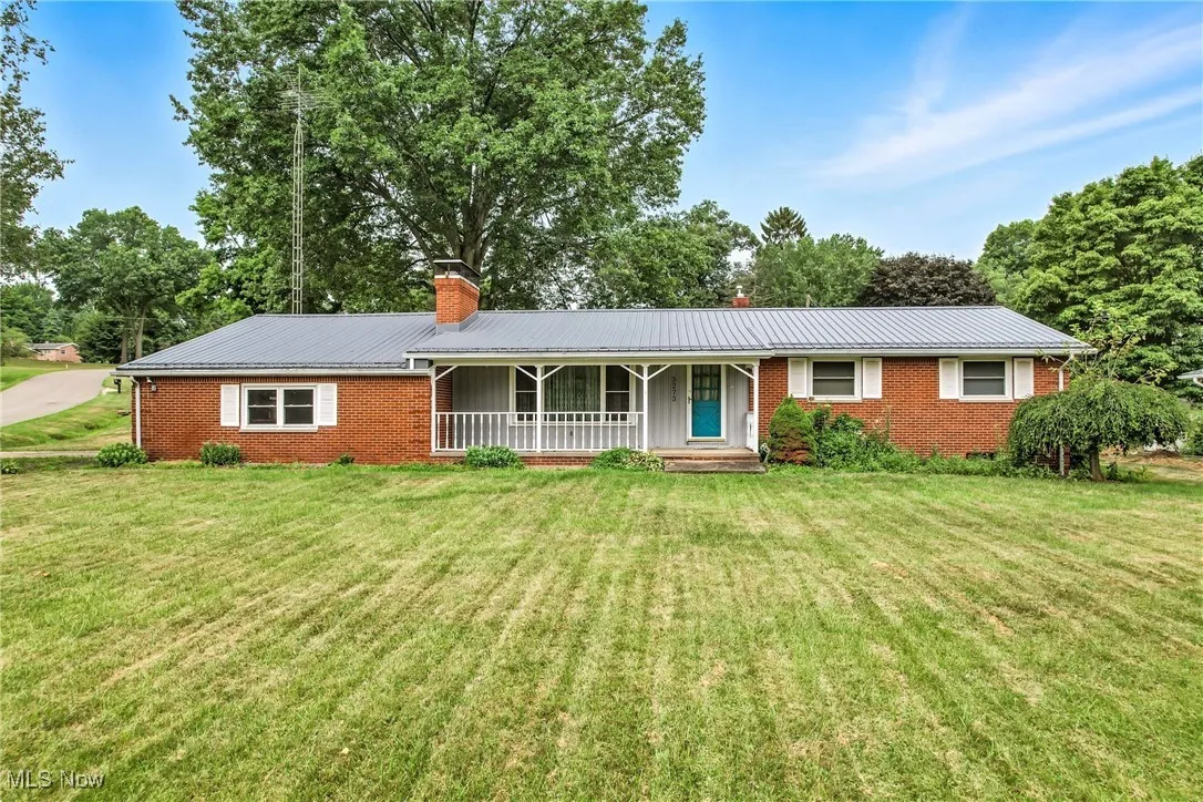 Single story home featuring a porch, a metal roof, brick siding, a chimney, and a front lawn