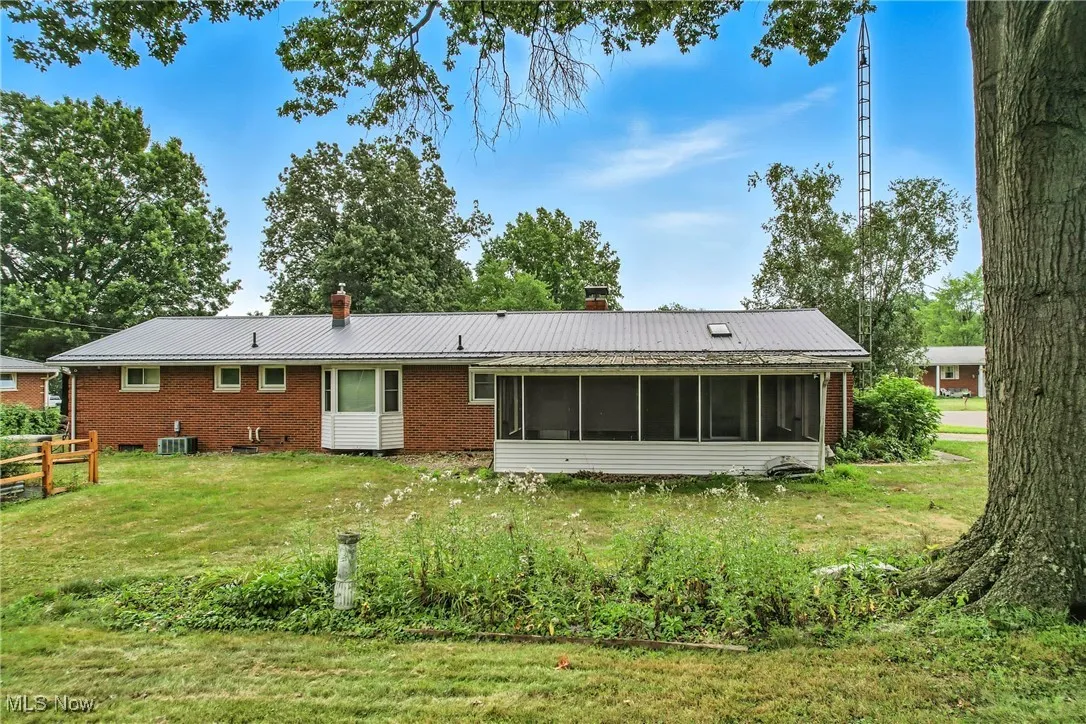Rear view of house featuring a chimney, a sunroom, brick siding, and a metal roof
