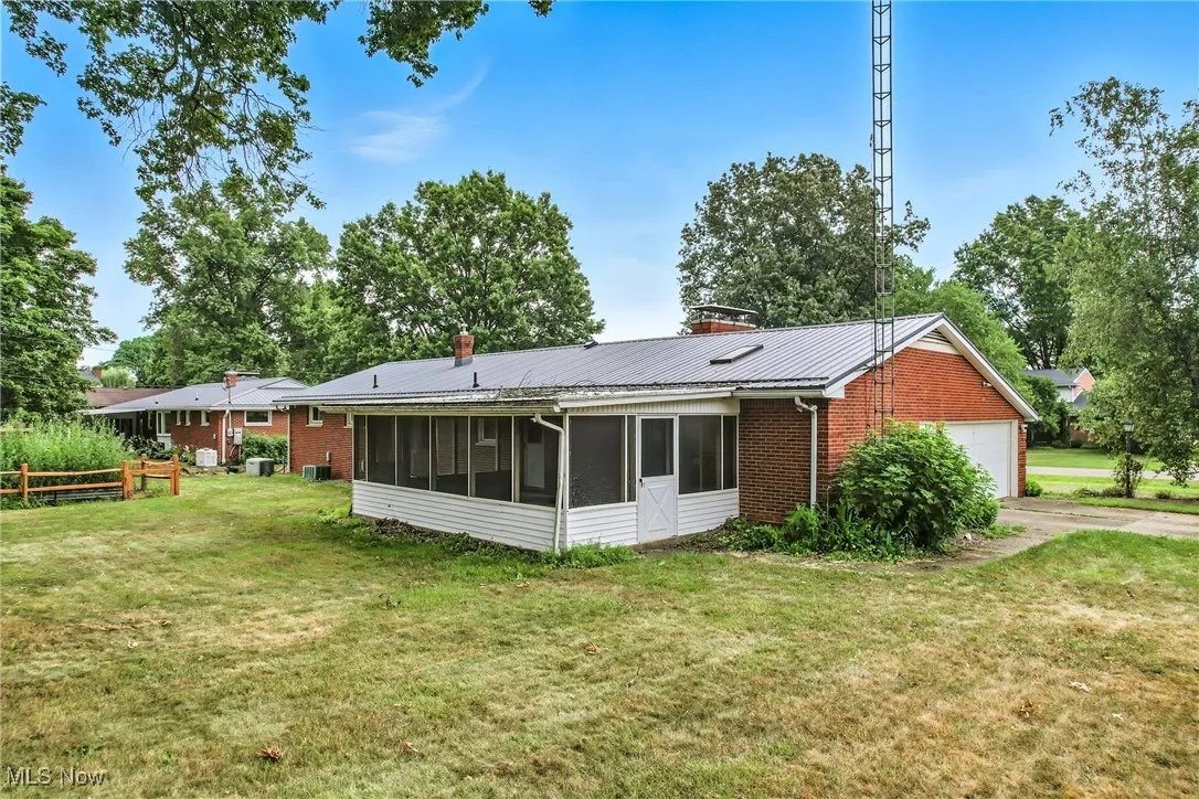Rear view of house featuring a sunroom, a garage, brick siding, a metal roof, and a chimney