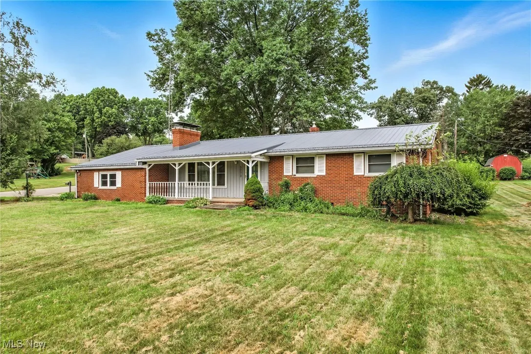 Single story home with a porch, a metal roof, a chimney, brick siding, and a front lawn