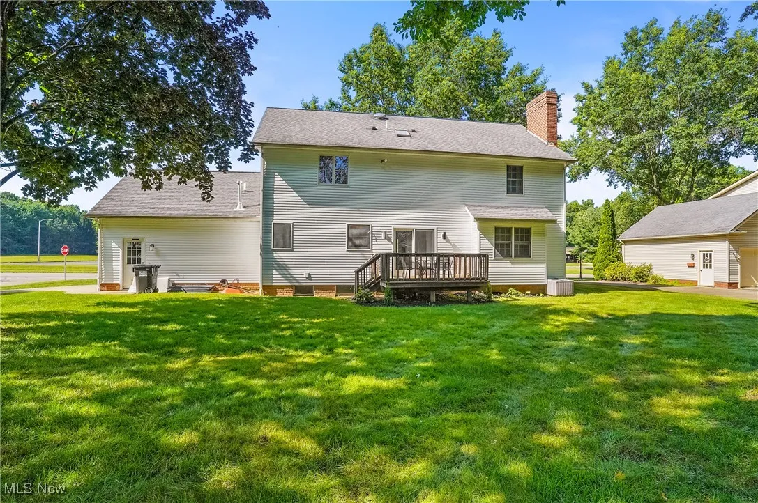 Back of house with a chimney, a lawn, a deck, and roof with shingles