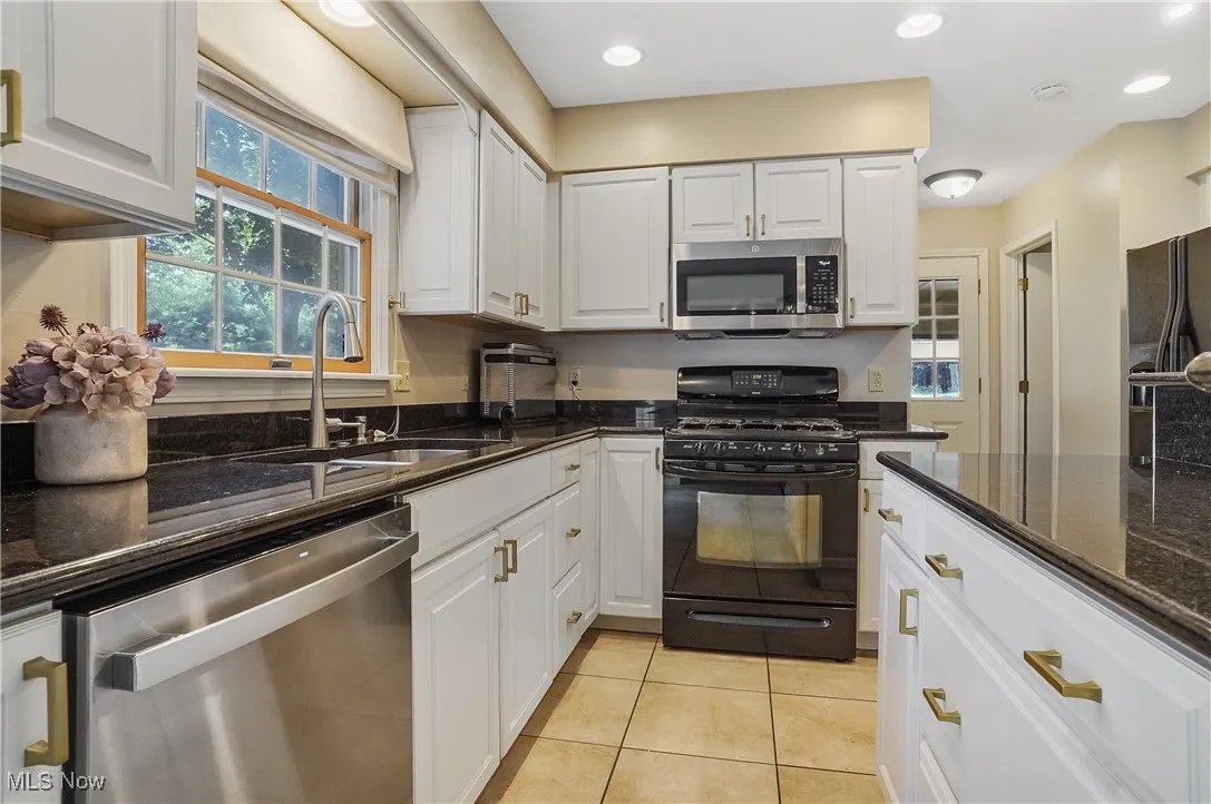 Kitchen featuring stainless steel appliances, light tile patterned floors, white cabinets, dark stone counters, and recessed lighting