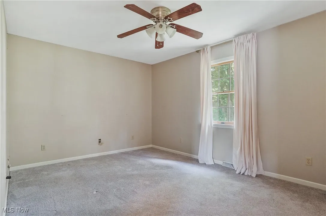 Carpeted empty room with ceiling fan and baseboards