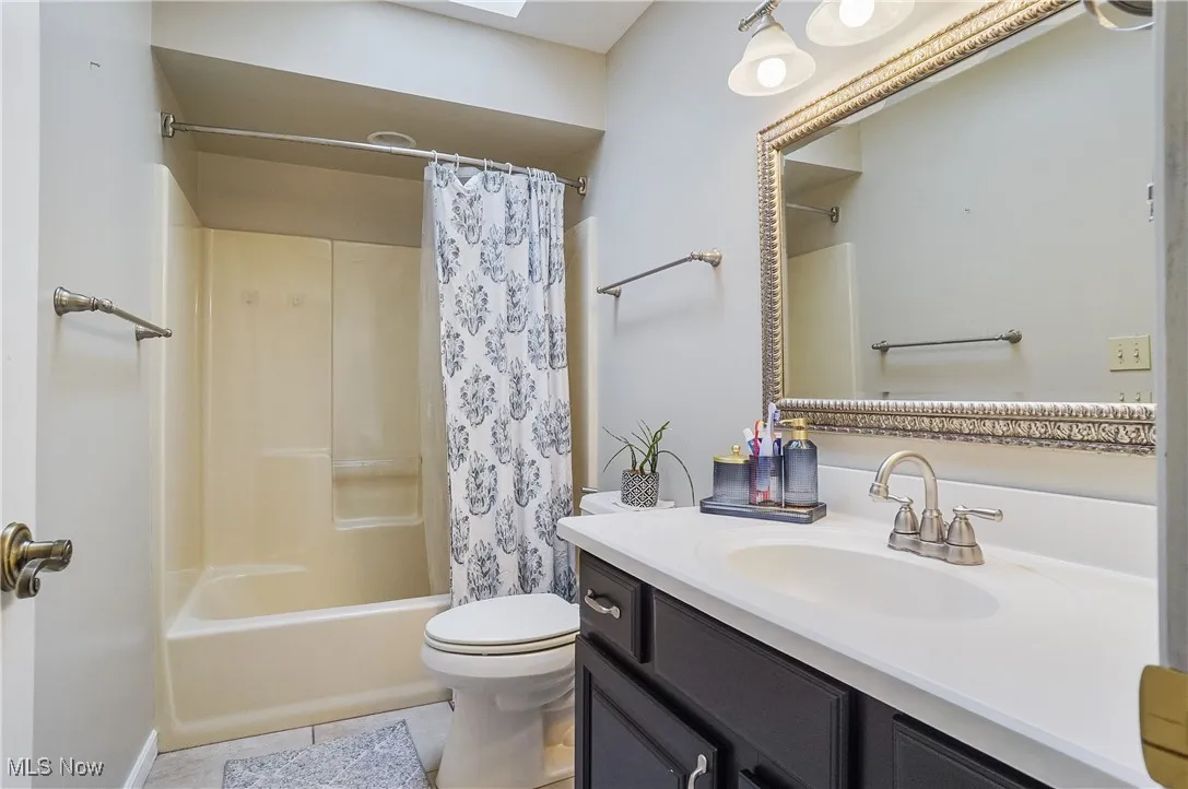 Bathroom with vanity, shower / bath combo with shower curtain, tile patterned flooring, and a skylight