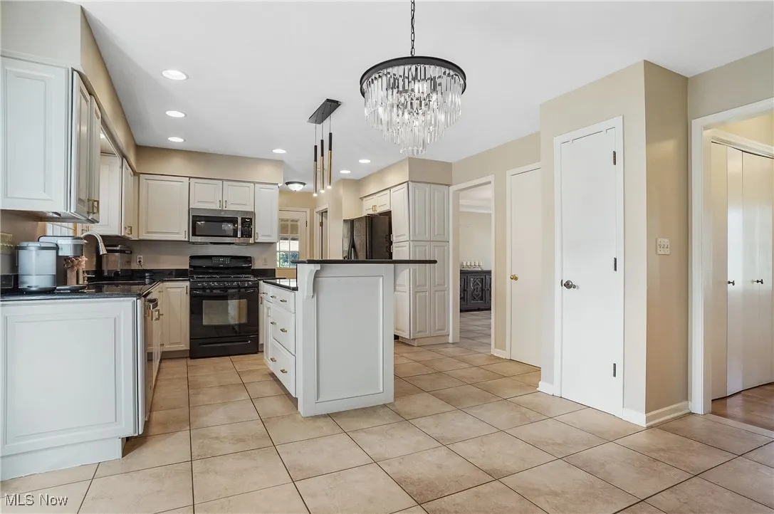 Kitchen with dark countertops, black appliances, light tile patterned floors, white cabinetry, and a chandelier