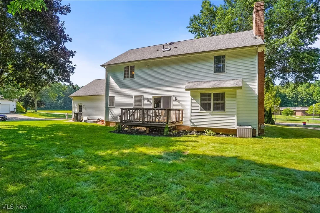 Back of property featuring a chimney, a lawn, a shingled roof, and a wooden deck
